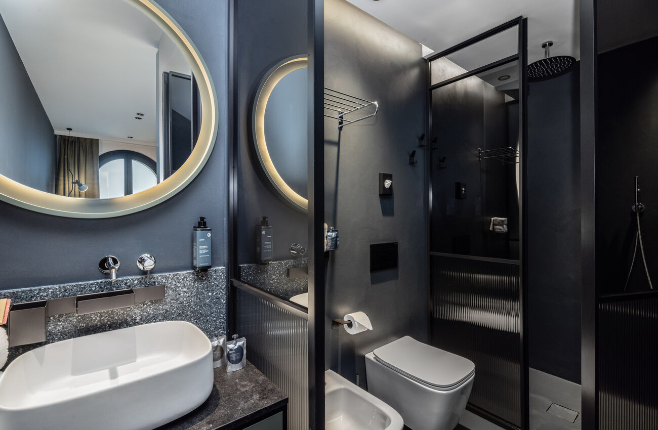Junior suite vista lago | La luce del lago attraversa lo spazio e ne rivela le geometrie, in un gioco tra materia, colori e profondità. La doccia walk-in completa l’ambiente come un gesto naturale. 