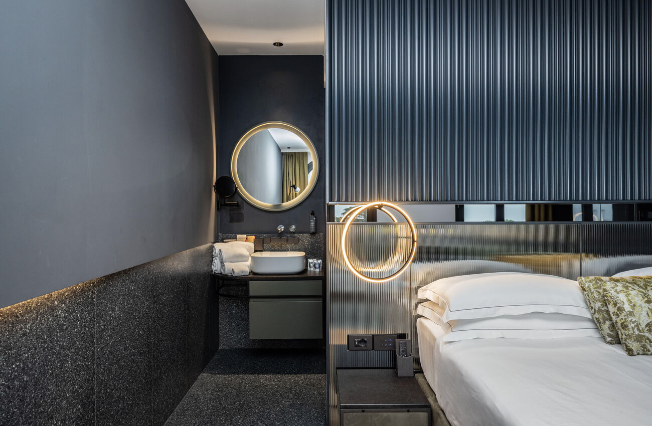 Junior suite vista lago | La luce del lago attraversa lo spazio e ne rivela le geometrie, in un gioco tra materia, colori e profondità. La doccia walk-in completa l’ambiente come un gesto naturale. 
